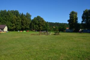 pole campingowe z ławkami i stołami na środku, w tle lasy